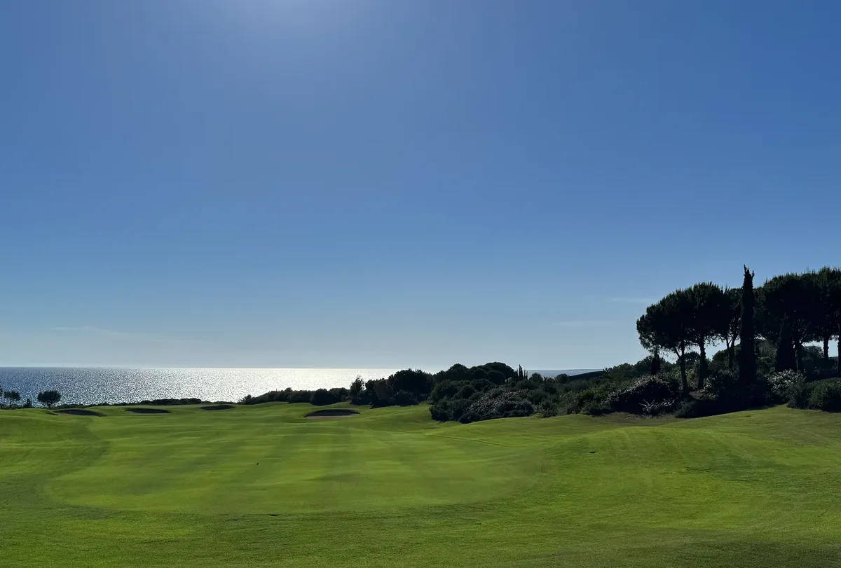 A golf fairway with bunkers, trees and a view of the sea